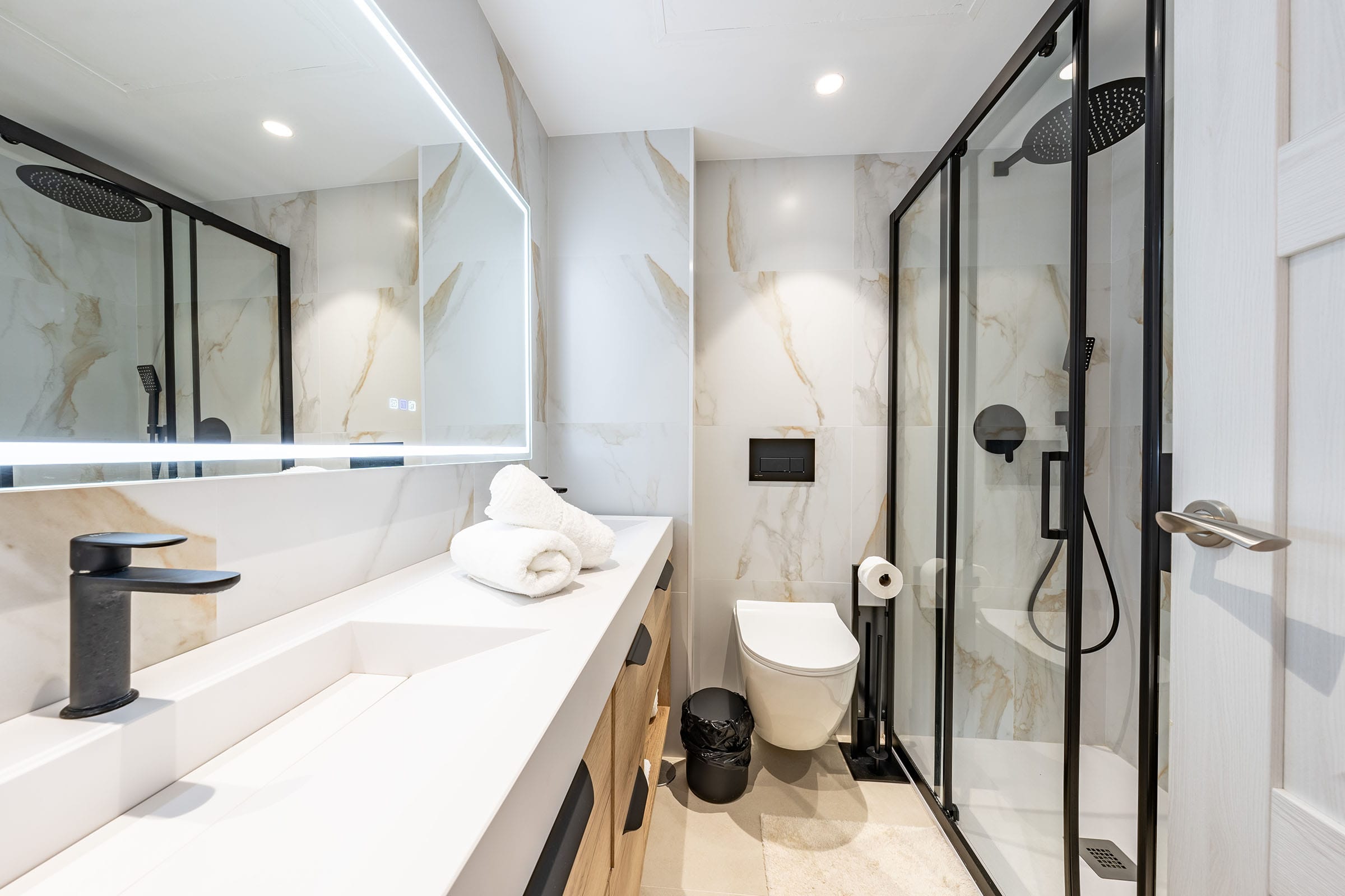 Modern bathroom with glass shower and LED mirror.