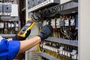 Technician testing electrical panel with multimeter.