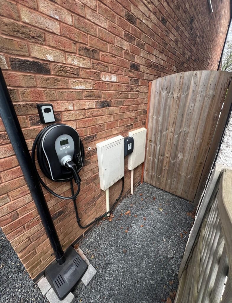 Electric vehicle charger on brick wall near gate.