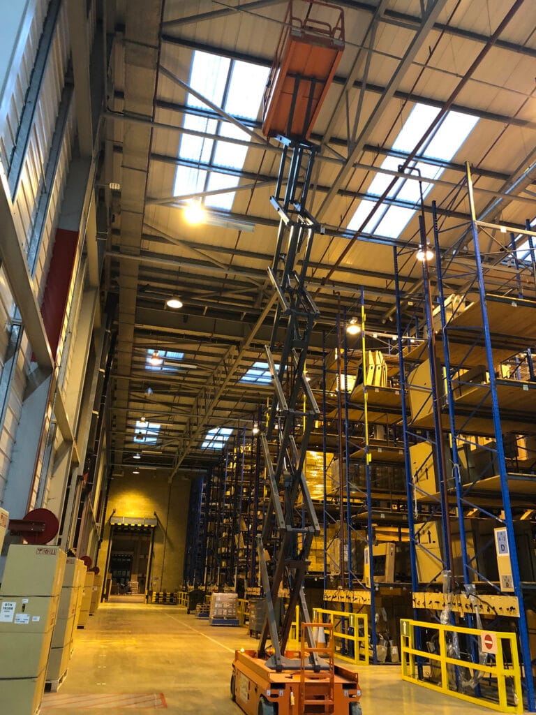 Scissor lift in spacious warehouse with high shelves.