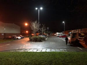 Nighttime car park with street lights and vehicles.