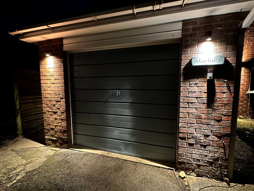 Illuminated garage door in brick wall at night.
