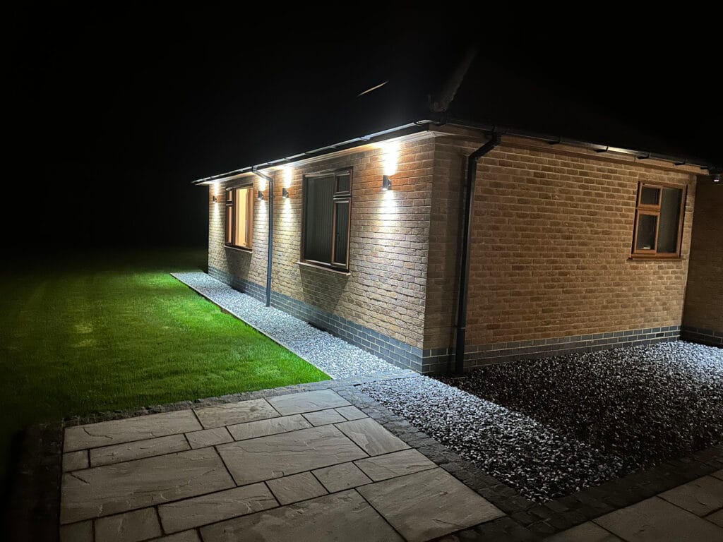 Lit pathway and grass beside brick house at night.